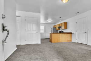 Great room featuring freestanding refrigerator, under cabinet range hood, carpet floors, a peninsula, and dark countertops