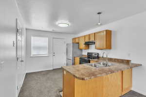 Kitchen with black / electric stove, under cabinet range hood, freestanding refrigerator, a sink, and baseboards