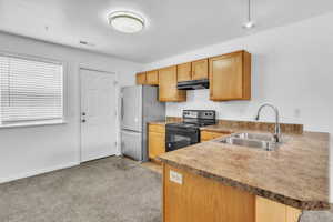 Kitchen featuring electric range, a sink, freestanding refrigerator, under cabinet range hood, and light colored carpet