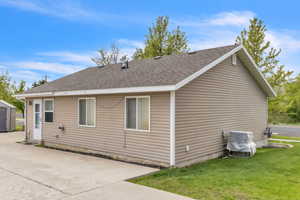 Back of property featuring a shingled roof, a lawn, and a patio area