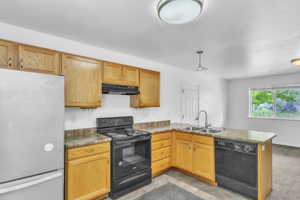 Kitchen featuring black appliances, a sink, under cabinet range hood, a peninsula, and dark countertops