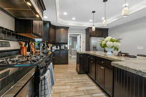 Kitchen with appliances with stainless steel finishes, wall chimney range hood, ornamental molding, decorative backsplash, and wood tiled floors.