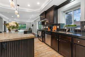 Kitchen featuring a sink, stainless steel appliances, under cabinet range hood, decorative backsplash, and dark brown cabinetry.