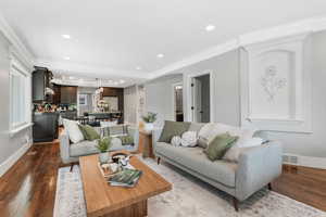 Living area featuring dark wood-style floors, recessed lighting, crown molding, arched walkways, and baseboards.
