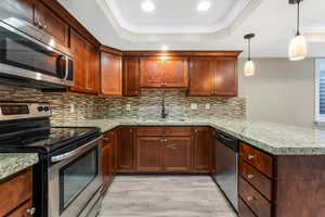 Kitchen featuring stainless steel appliances, a sink, a tray ceiling, a peninsula, and light wood finished floors.