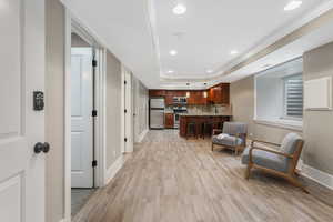 Living area featuring light wood finished floors, a raised ceiling, baseboards, and recessed lighting.