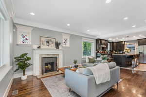 Living area with ornamental molding, dark wood-style flooring, a tiled fireplace, recessed lighting, and baseboards.