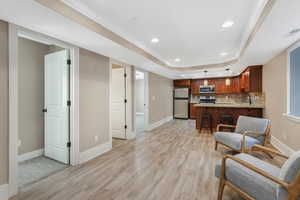 Living area featuring light wood-type flooring, baseboards, a raised ceiling, and recessed lighting.
