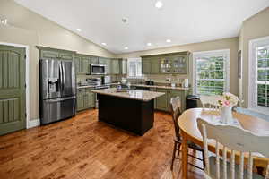 Kitchen featuring stainless steel appliances, green cabinets, vaulted ceiling, recessed lighting, and light wood finished floors