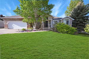 View of front facade with an attached garage, a front yard, concrete driveway, brick siding, and roof with shingles