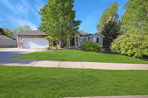 View of front facade featuring a garage, a front lawn, concrete driveway, brick siding, and roof with shingles