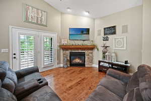 Living area featuring a stone fireplace, wood finished floors, baseboards, and a towering ceiling