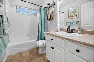Bathroom with toilet, shower / tub combo with curtain, vanity, and stone finish flooring