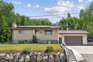 View of front of house featuring solar panels, driveway, an attached garage, and metal roof