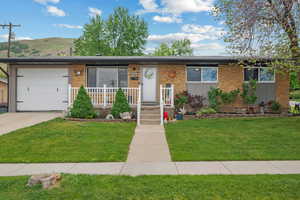 View of front facade featuring a front lawn, an attached garage, a mountain view, concrete driveway, and brick siding