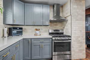 Kitchen with stainless steel gas stove, wall chimney exhaust hood, light countertops, and backsplash