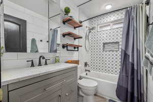 Full bathroom with shower / bath combo with shower curtain, toilet, vanity, and tasteful backsplash
