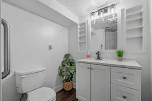 Bathroom with wood finished floors, toilet, baseboards, vanity, and a textured ceiling