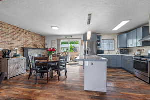 Kitchen with stainless steel appliances, dark wood finished floors, brick wall, a textured ceiling, and decorative light fixtures