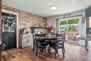 Dining room featuring brick wall, a textured ceiling, and dark wood-style flooring