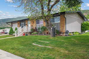 View of front of home featuring board and batten siding, a mountain view, a front lawn, and brick siding