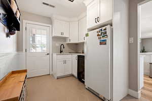 Kitchen featuring freestanding refrigerator, light countertops, a sink, white cabinets, and backsplash