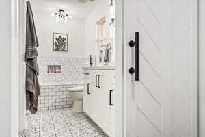 Full bathroom with tile walls, toilet, tiled bath, vanity, and wainscoting