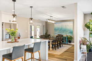 Kitchen featuring stainless steel fridge, light wood-style flooring, a breakfast bar, white cabinets, and pendant lighting
