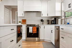 Kitchen featuring stainless steel appliances, custom range hood, and white cabinets