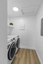 Laundry room with attic access, washing machine and dryer, light wood-style flooring, baseboards, and electric panel