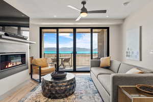 Living area featuring wood finished floors, a glass covered fireplace, ceiling fan, recessed lighting, and a water view