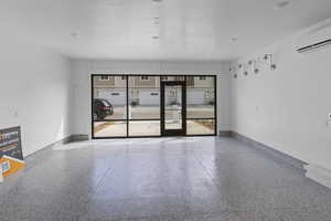 Empty room featuring speckle patterned floor, a wall mounted air conditioner, and baseboards