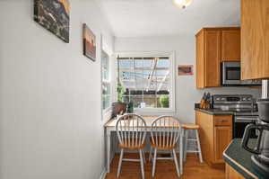 Kitchen featuring stainless steel appliances, light wood-style floors, brown cabinets, baseboards, and dark countertops