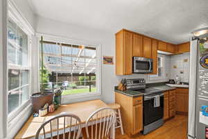 Kitchen featuring stainless steel appliances, light wood-style floors, a sink, brown cabinets, and dark countertops