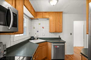 Kitchen featuring appliances with stainless steel finishes, a sink, dark countertops, decorative backsplash, and light wood-style flooring