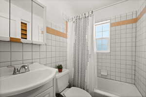 Full bathroom with tile walls, toilet, shower / tub combo with curtain, tasteful backsplash, and vanity