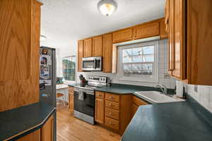 Kitchen with appliances with stainless steel finishes, a sink, a textured ceiling, brown cabinets, and dark countertops