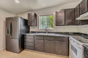 Kitchen featuring stainless steel refrigerator with ice dispenser, white range with electric stovetop, a sink, dark brown cabinets, and recessed lighting