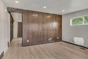 Empty room with light wood finished floors, recessed lighting, wood walls, and baseboards