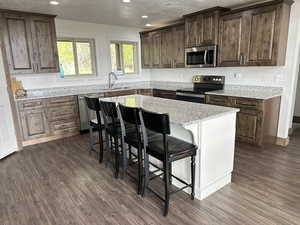 Kitchen featuring appliances with stainless steel finishes, a sink, dark wood-style floors, recessed lighting, and a kitchen bar