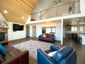 Living area with high vaulted ceiling, a ceiling fan, wood ceiling, a fireplace, and dark wood finished floors