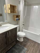 Bathroom with wood finished floors, toilet, shower / tub combo with curtain, and vanity