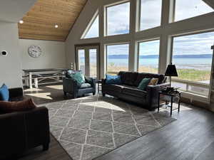 Living area with high vaulted ceiling, a water view, healthy amount of natural light, dark wood finished floors, and wooden ceiling