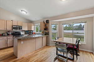Kitchen with appliances with stainless steel finishes, light brown cabinetry, a peninsula, a sink, and light wood finished floors