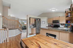 Kitchen with appliances with stainless steel finishes, open shelves, light brown cabinets, vaulted ceiling, and light wood finished floors