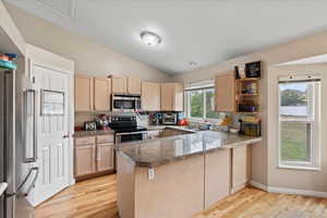 Kitchen featuring appliances with stainless steel finishes, light brown cabinetry, a peninsula, a sink, and light wood finished floors