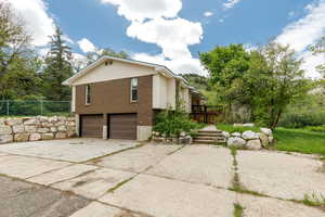 View of property exterior with a garage, brick siding, driveway, and fence
