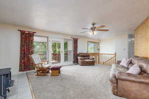 Living room with ceiling fan, light tile patterned floors, baseboards, and a wood stove