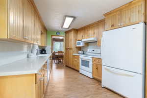 Kitchen featuring white appliances, under cabinet range hood, light wood finished floors, a sink, and tasteful backsplash