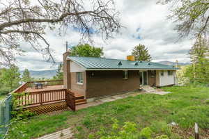 Rear view of property featuring brick siding, a chimney, a deck with mountain view, metal roof, and a lawn